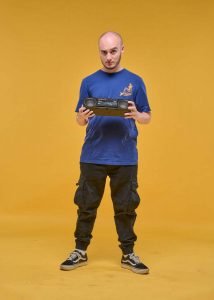 portrait of DJ holding small ghetto blaster on yellow background